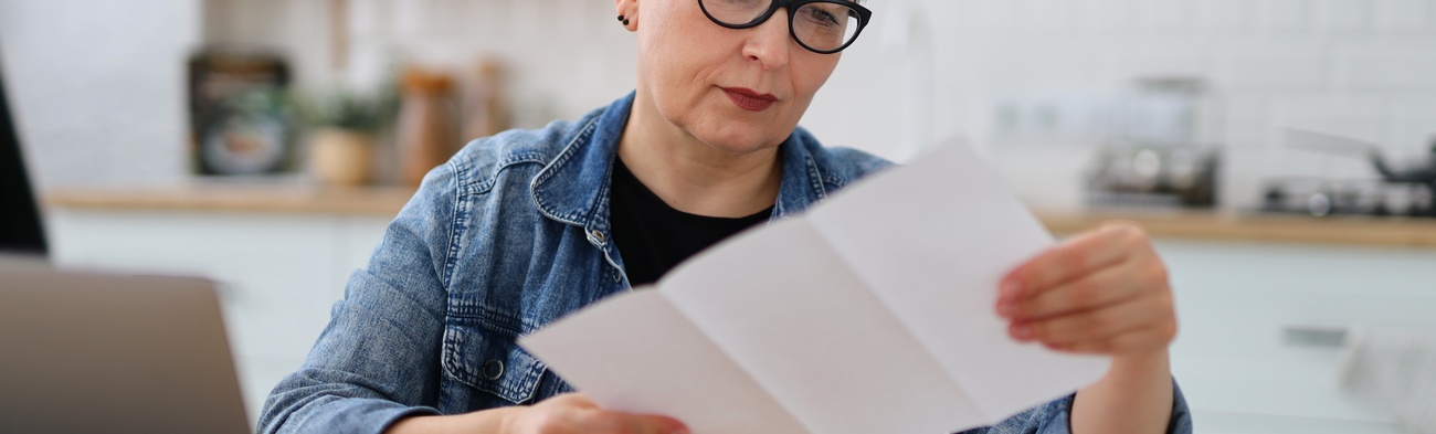 Ältere Frau mit Brille liest in der Küche die Rechnung.