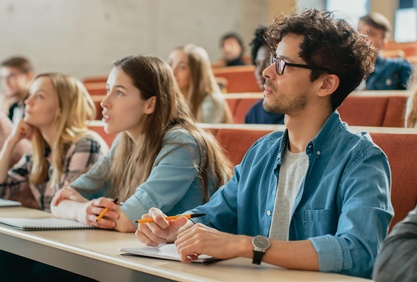 Mehrere Studierende sitzen in einem Hörsaal und hören einem Dozenten zu. 